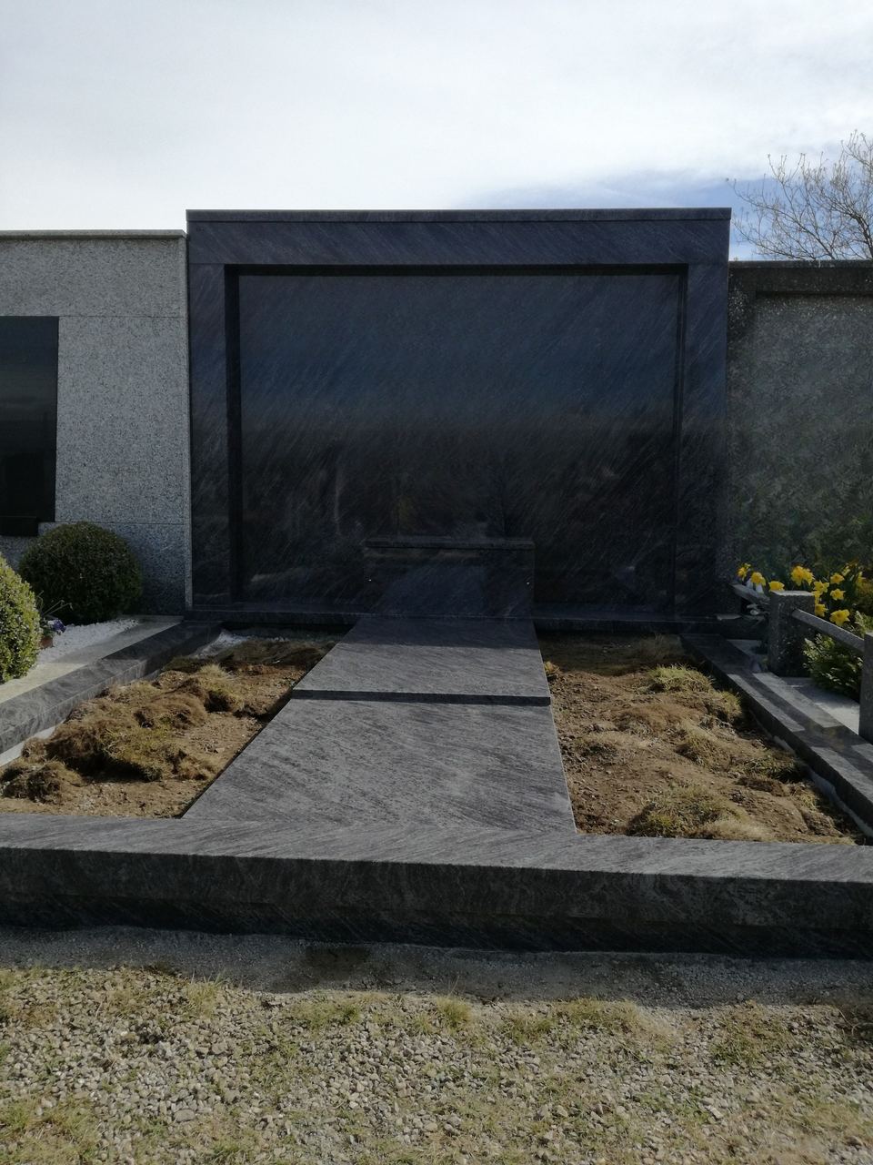 Gruft an der Mauer mit Abdeckung aus dunklem Granit und eingemeißeltem Kreuz