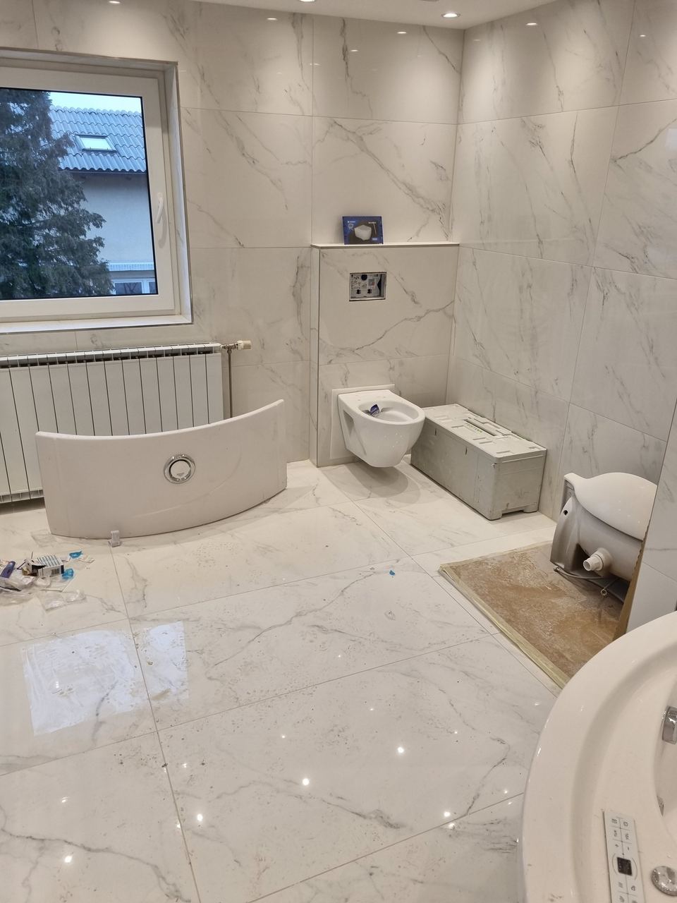 Bad mit Wand und Bodenverkleidung aus weißen Platten mit grauen Adern