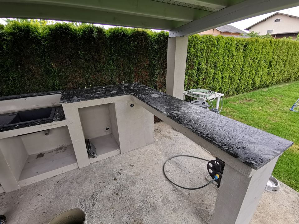 Sommerküche mit Arbeitsplatte aus Granit mit weißen Körnern unter einem Vordach